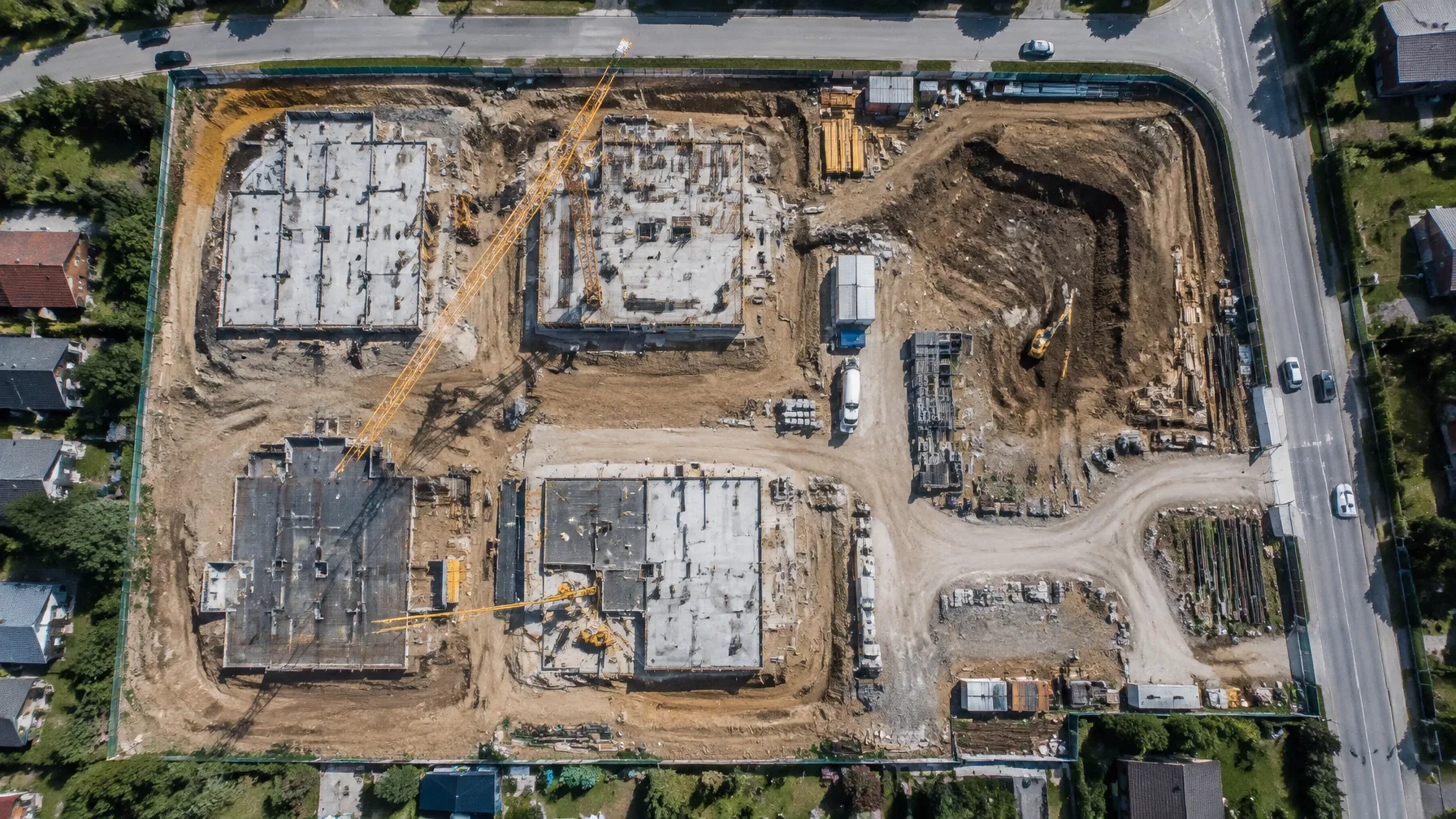 Top-down aerial view of a construction site with concrete slabs, cranes, earthworks and surrounding roads